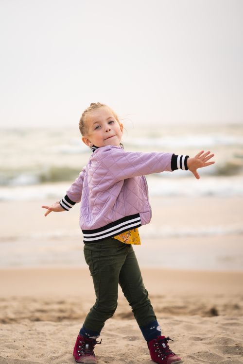 Free A carefree young girl in a jacket dances happily on Grand Haven beach. Stock Photo