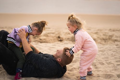 Free Dad playing with his daughters on a sandy beach, capturing joyful family bonding moments. Stock Photo