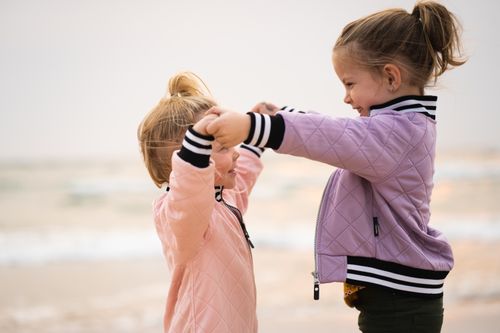 Free Two young sisters in pastel jackets play joyfully on Grand Haven Beach, Michigan. Stock Photo