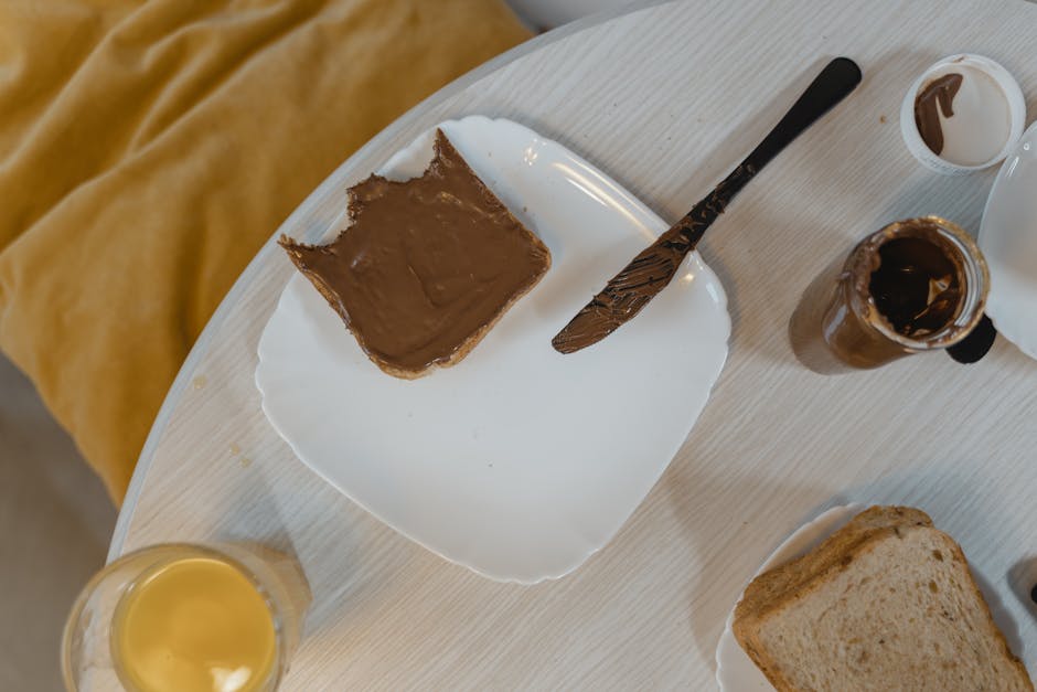 Overhead view of a breakfast table with bread and chocolate spread, knife, and a jar.