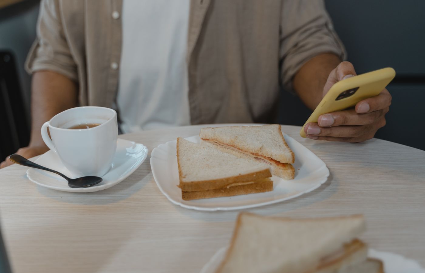 Casual breakfast scene with coffee, sandwiches, and a smartphone in hand.
