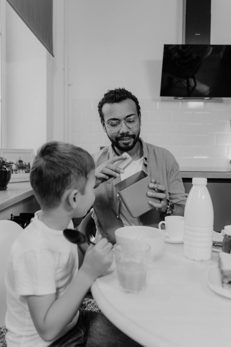 Father And Son Sitting By Table In Kitchen