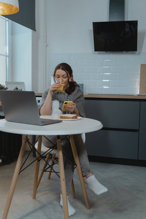 Free Woman Using Cellphone While Eating Snack Stock Photo