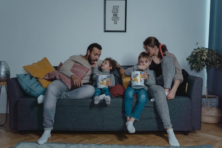 Family Sitting On Blue Sofa Eating Popcorn