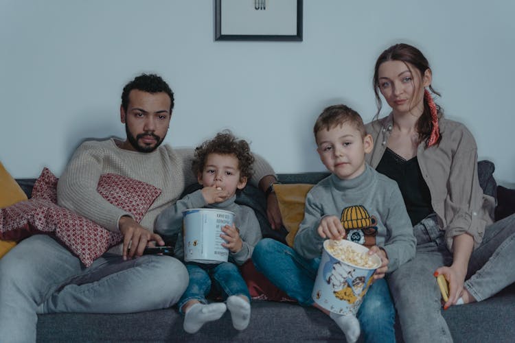 Family Sitting On Blue Sofa Eating Popcorn