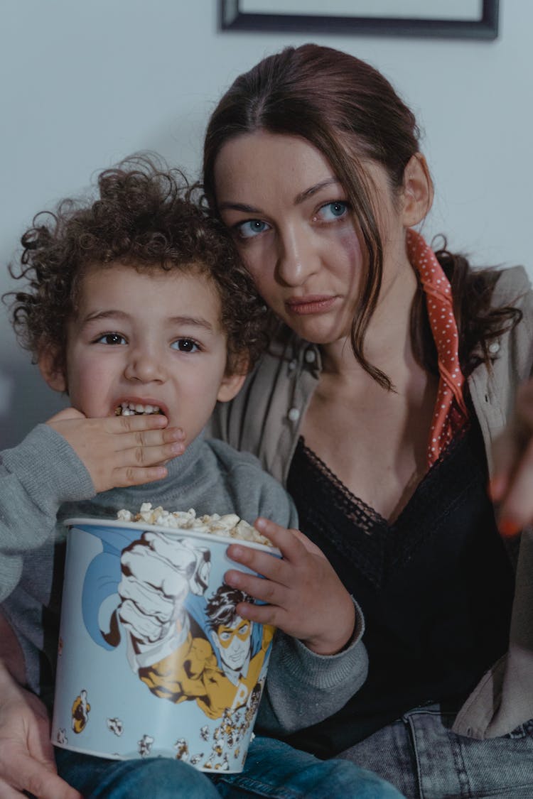 A Boy Eating Popcorn With His Mother On His Side