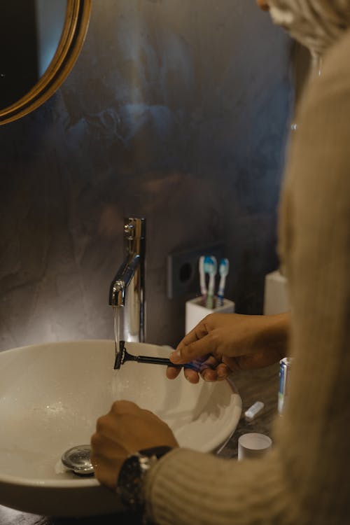 Person Washing a Shaver in a Bathroom Sink