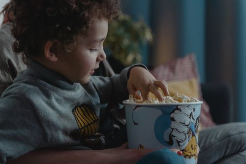 Free A young child enjoys a bowl of popcorn while sitting indoors. Stock Photo