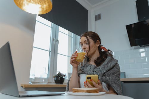 Free A Woman Using a Smartphone while Drinking a Glass of Drink Stock Photo
