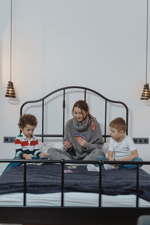 Free A joyful mother spending quality time with her two sons playing cards on a bed in a cozy room. Stock Photo