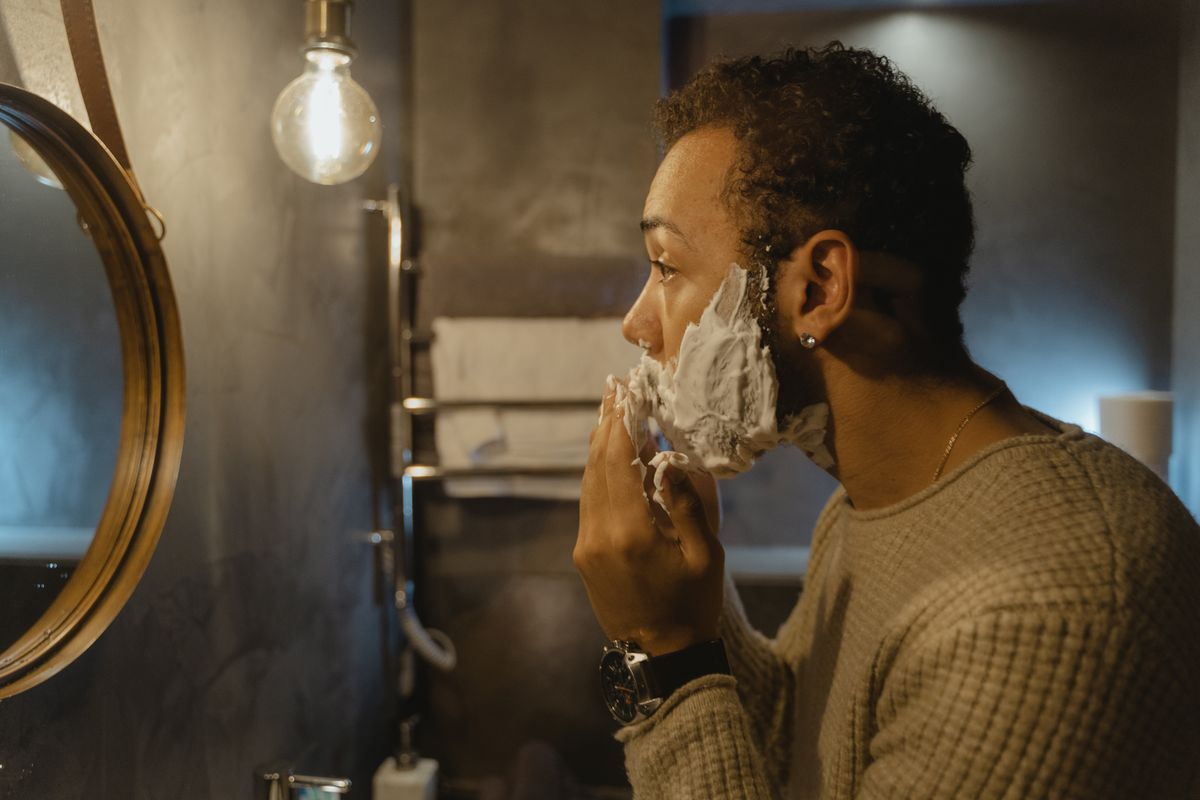 Homem aplicando creme de barbear diante do espelho
