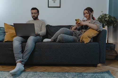 A Man and Woman Sitting on the Couch while Using their Gadgets