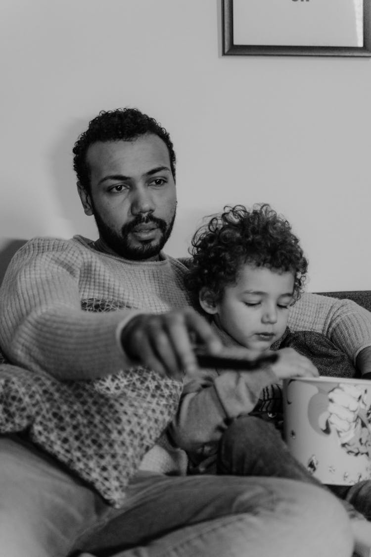 A Father  And Son Watching TV With A Bucket Of Popcorn