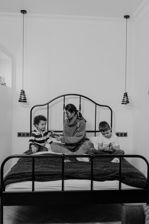 Free Grayscale Photo of Woman and Boys Sitting on Bed Stock Photo