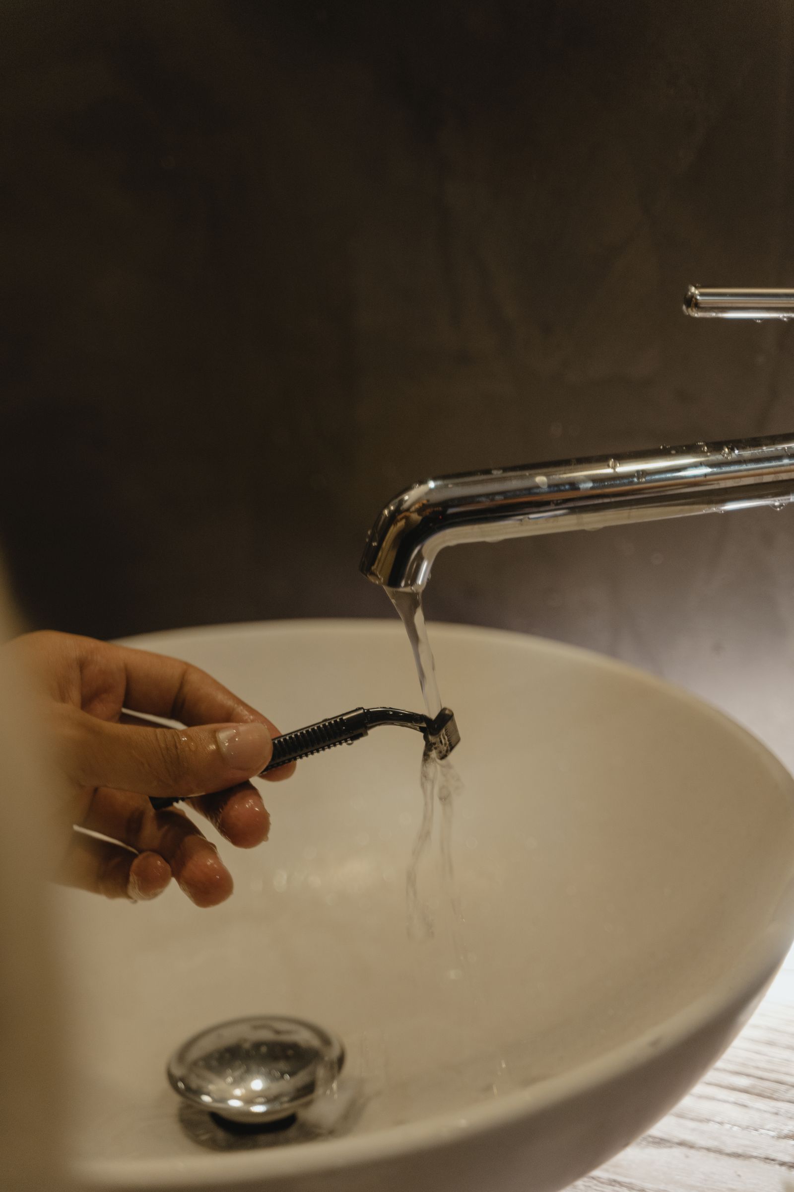 Hand washing a grooming shaver under running water at a bathroom sink