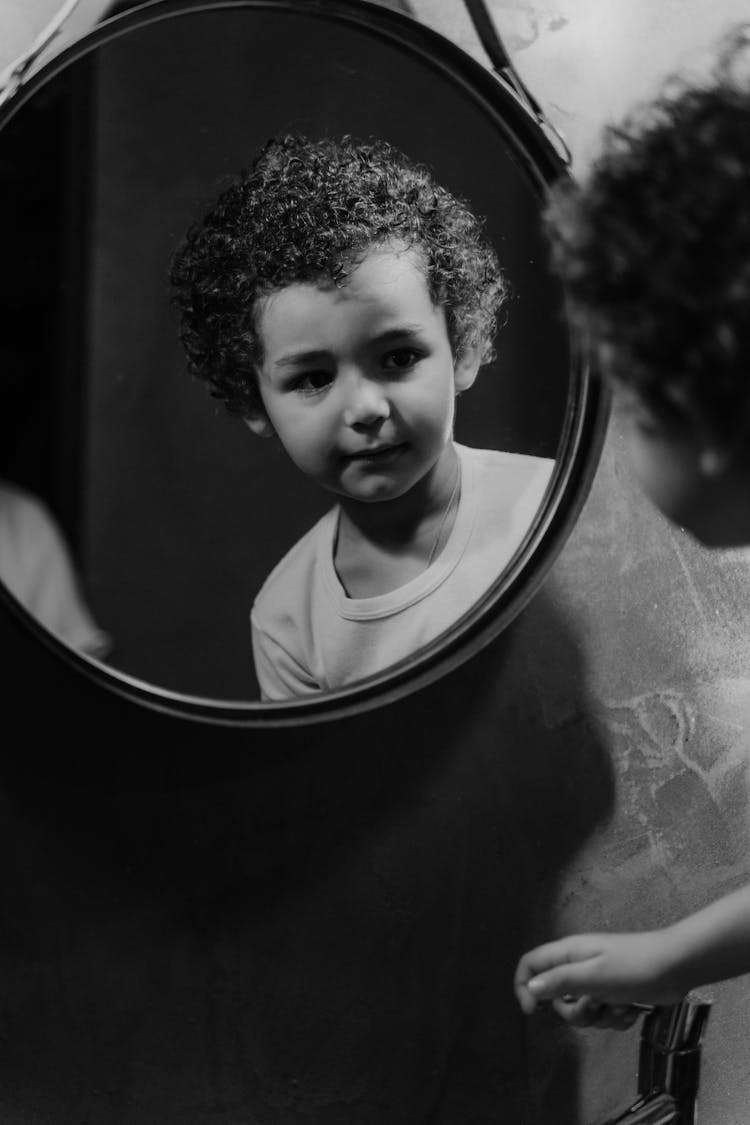 Grayscale Photography Of A Kid Looking At The Round Mirror