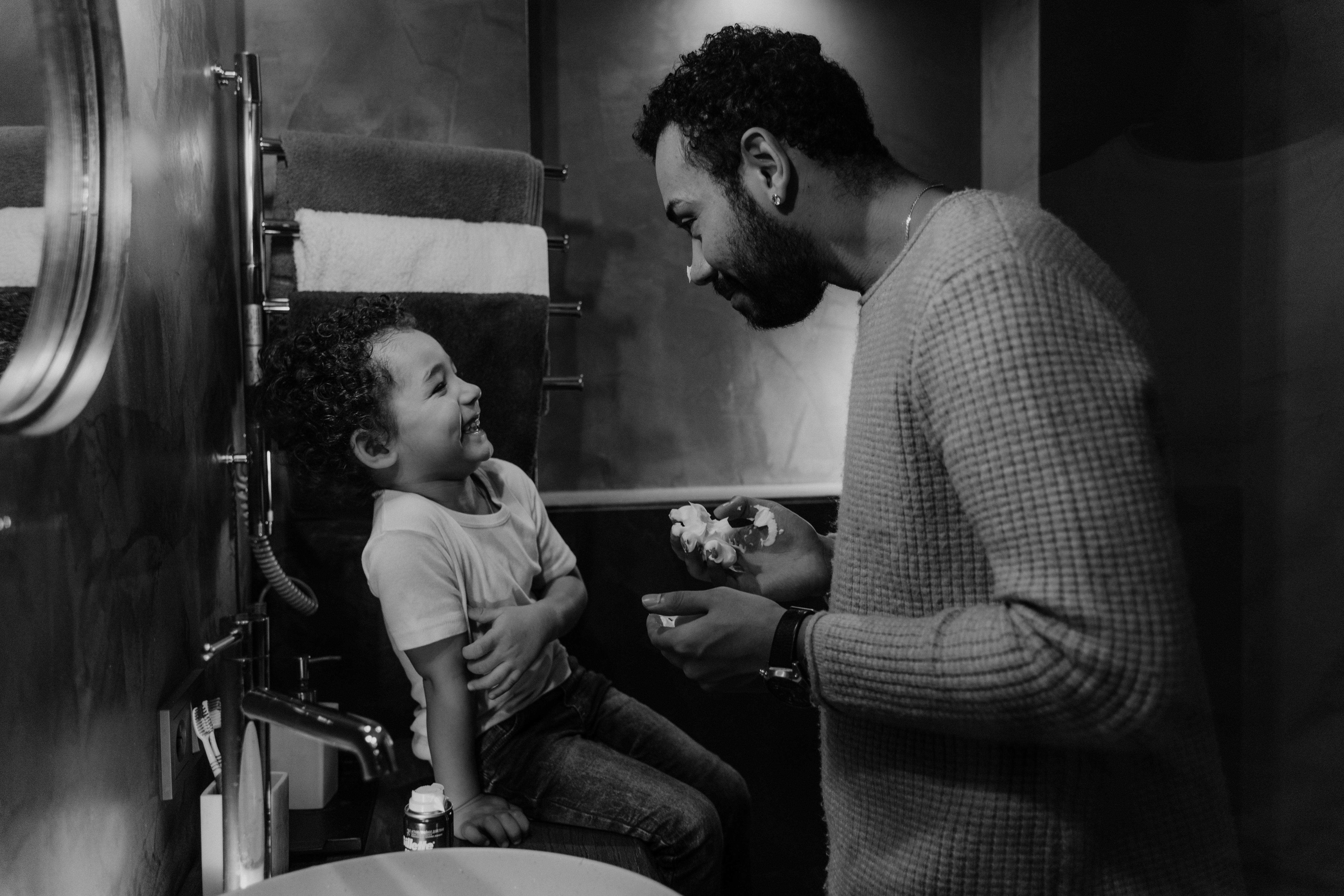 Father and son enjoy bonding time in a cozy bathroom setting, captured in black and white.