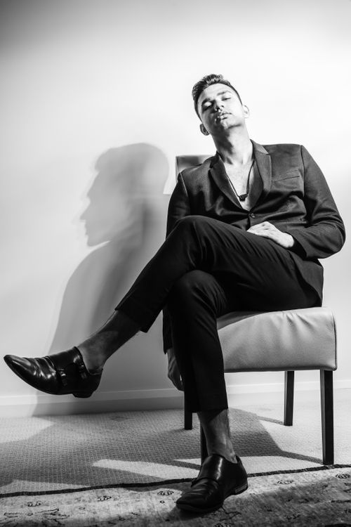 Free Black and white full body of stylish young male in formal black suit and shoes sitting on comfortable white leather chair and looking at camera Stock Photo