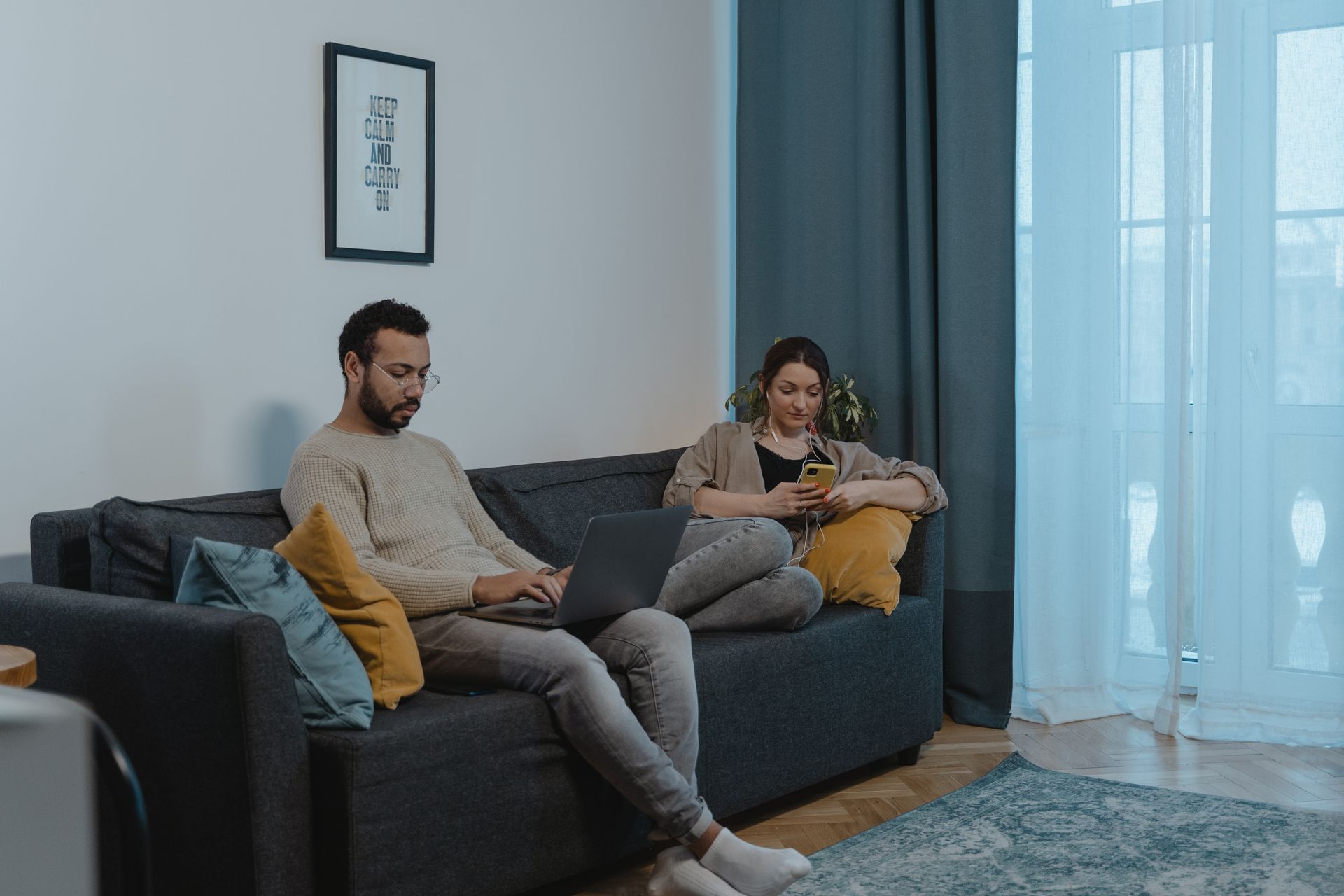 A couple sitting on a sofa using a laptop and smartphone in a modern living room.