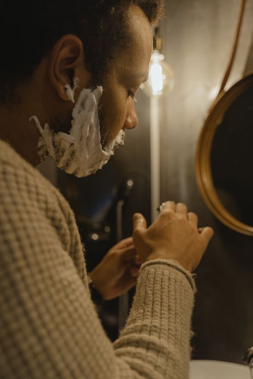 Free Side view of a man applying shaving cream, creating a homey and warm bathroom ambience. Stock Photo