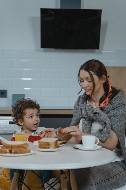 Free A woman and child sharing a snack at the dining table, fostering bonding moments. Stock Photo