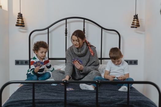 Mother and children play cards in cozy bedroom, enjoying quality bonding time.