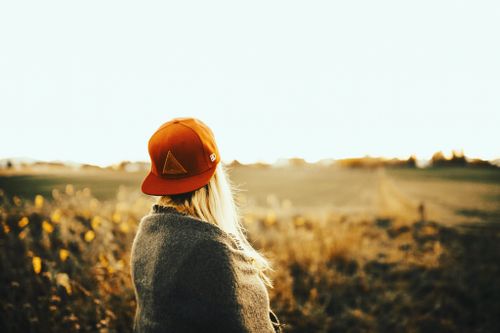 Free A woman with blonde hair and a cap enjoys a sunny field at golden hour, embracing nature and tranquility. Stock Photo