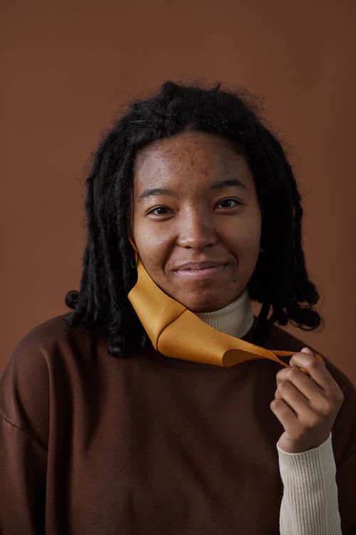 Free A young woman with curly hair and acne removing a face mask while smiling indoors. Stock Photo