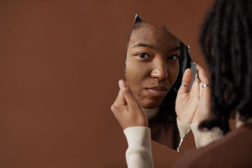 Free A woman holding and looking into a broken mirror, reflecting on self image and identity. Stock Photo