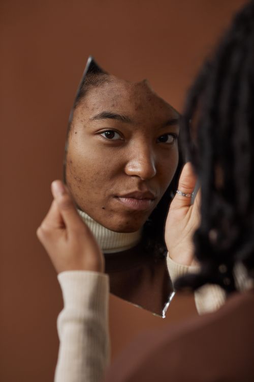Free A young woman holds a broken mirror, her reflection showing a calm expression against a brown background. Stock Photo