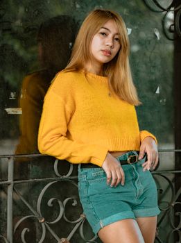 Young woman in a yellow sweater posing confidently outdoors. Fashion-forward and relaxed vibe.