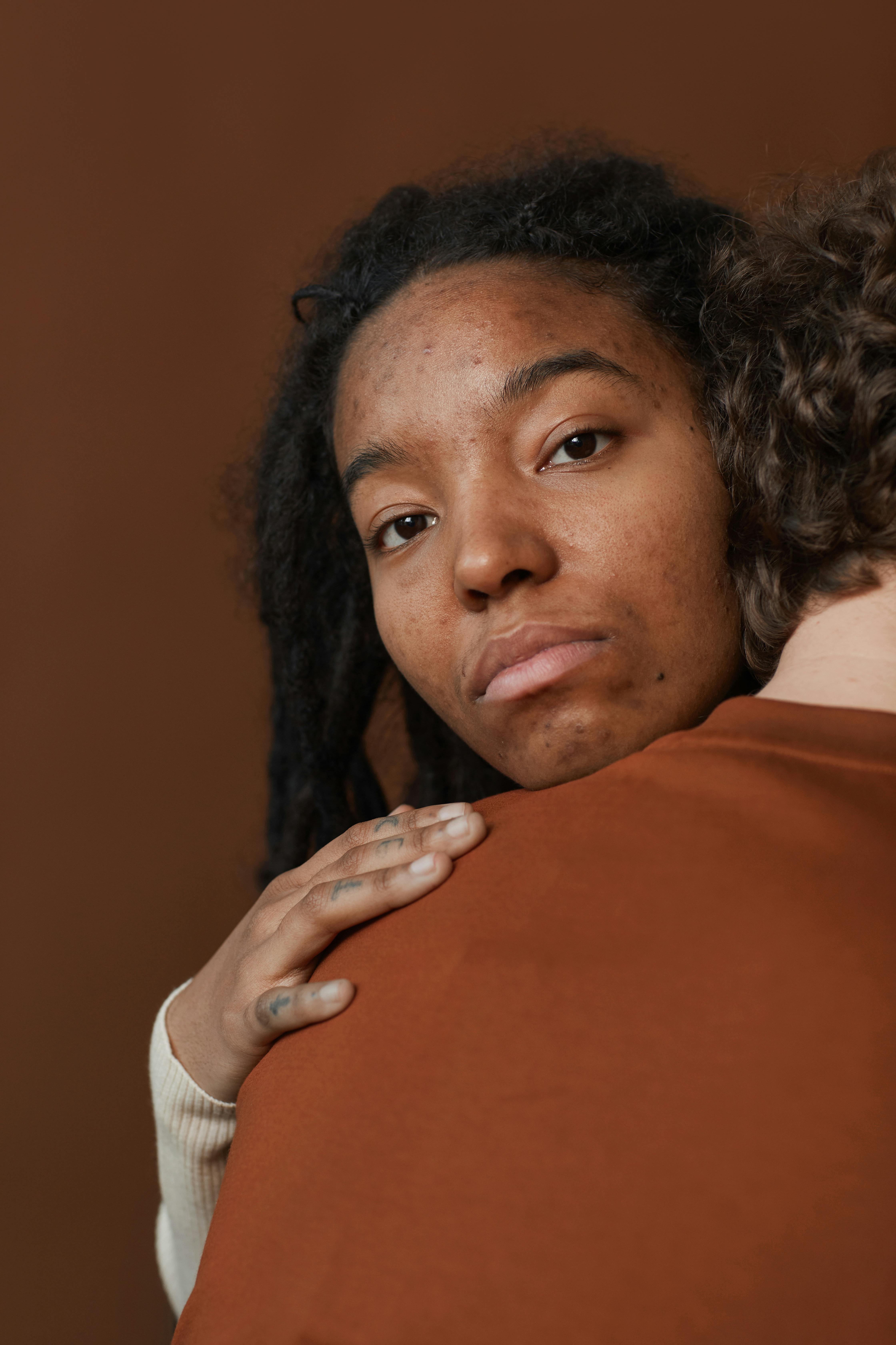 An intimate portrait of a young woman with a thoughtful expression, embracing a companion in a studio setting.