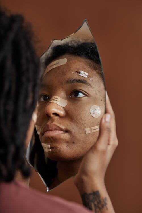 A Woman with Band Aids on Face Looking in a Broken Mirror