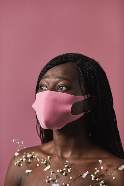 Elegant portrait of a young black woman wearing a pink face mask with delicate flowers on a pink background.