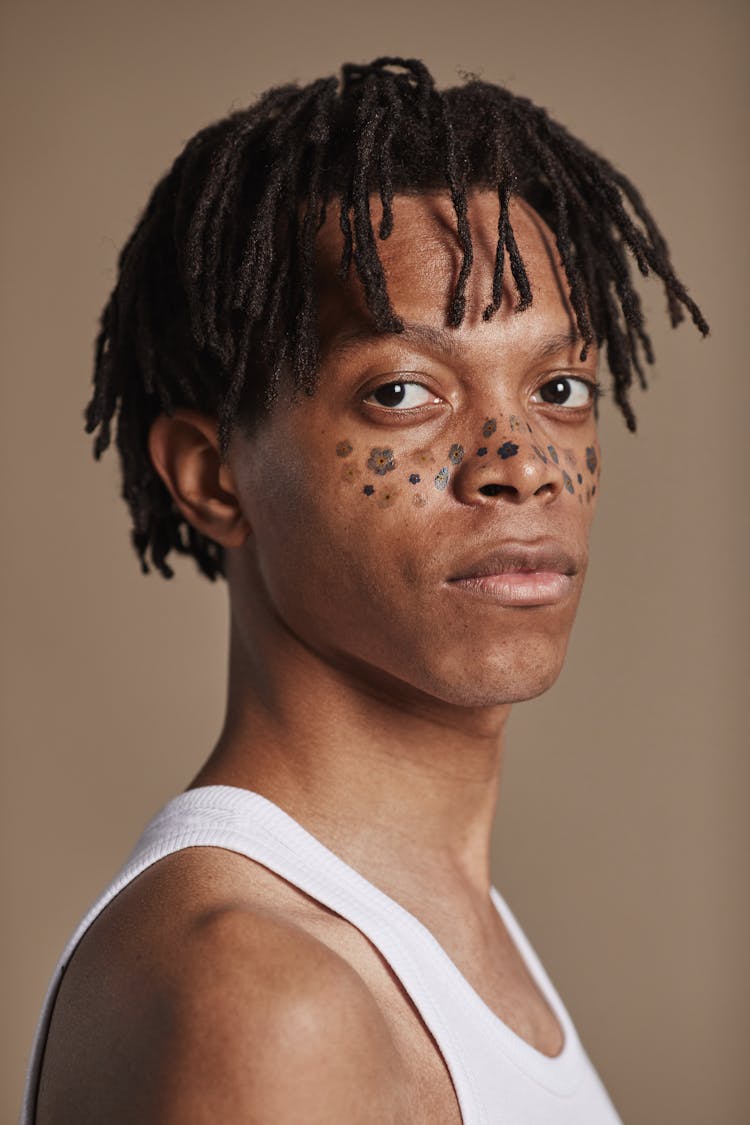 A Man In White Tank Top With Black Flowers Tattooed On Face