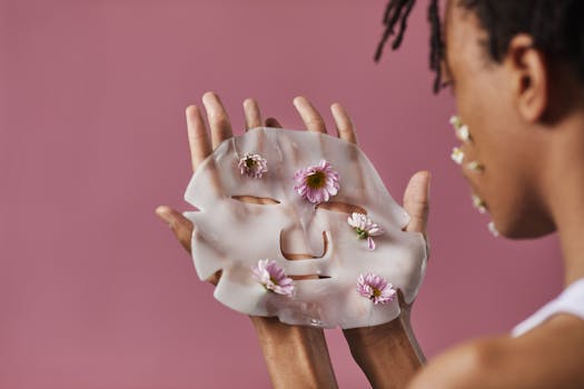 Close-up of hands holding a floral sheet mask with daisies against a pink background.