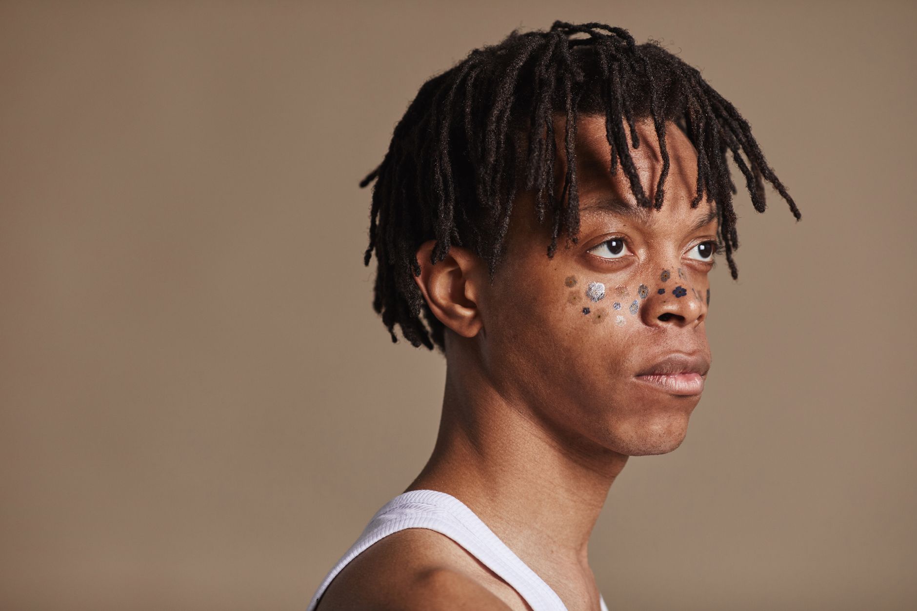 Side profile of a man with dreadlocks and artistic facial paint in a studio setting.