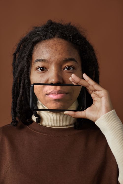 Free A unique portrait highlighting a smartphone as a reflection of a woman's face against a brown background. Stock Photo