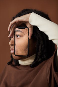 Artistic portrait of a person with dreadlocks framed by a smartphone, highlighting facial textures.