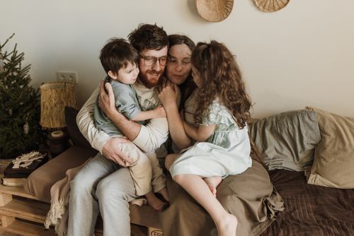 Free A joyful family of four embracing on a cozy couch, showcasing love and warmth indoors. Stock Photo