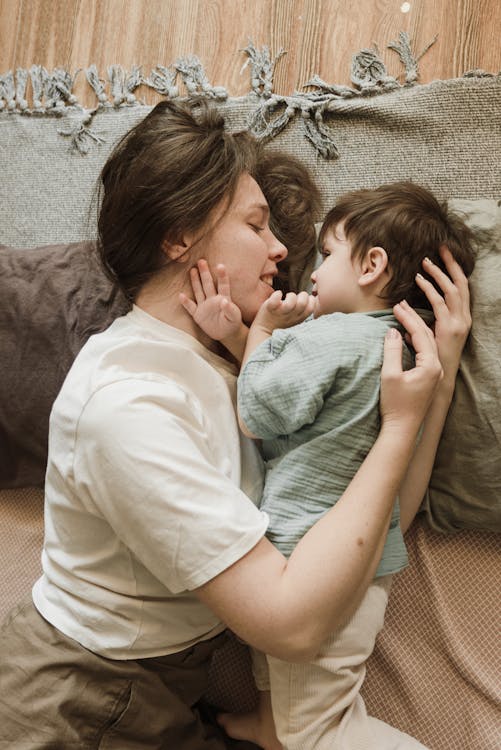 Happy young mother embracing adorable little son while lying on floor
