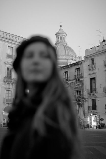 Blurry silhouette of a woman with Catania's historic architecture in grayscale background.