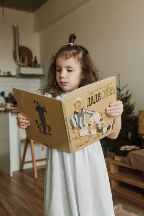 Free Young girl reading a children's book in a cozy indoor setting. Stock Photo