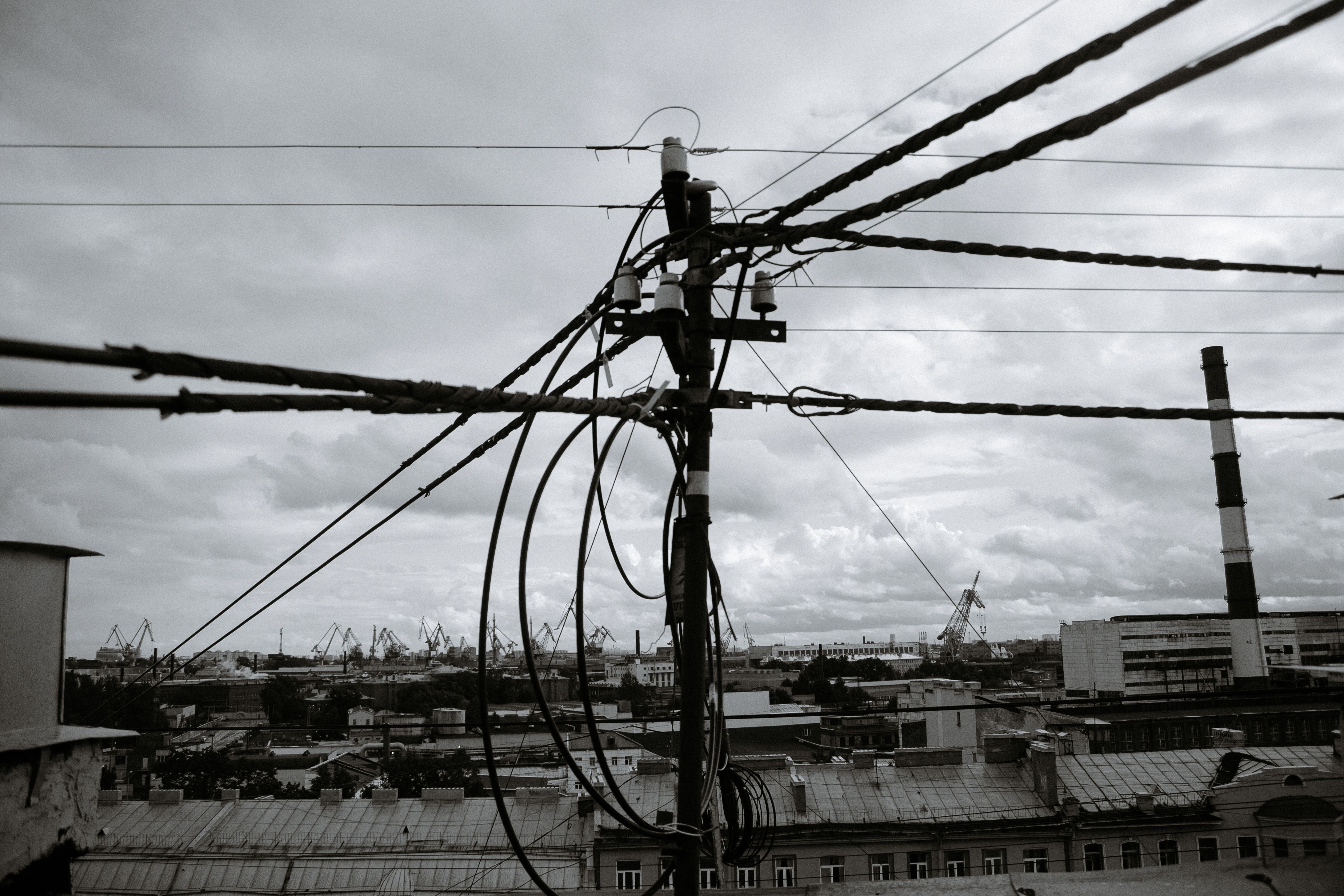 Black-and-white view of tangled power lines against an urban industrial landscape with cranes.