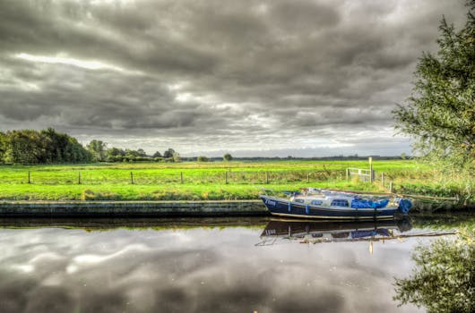A peaceful European river scene with a sailboat, lush greenery, and dramatic clouds.
