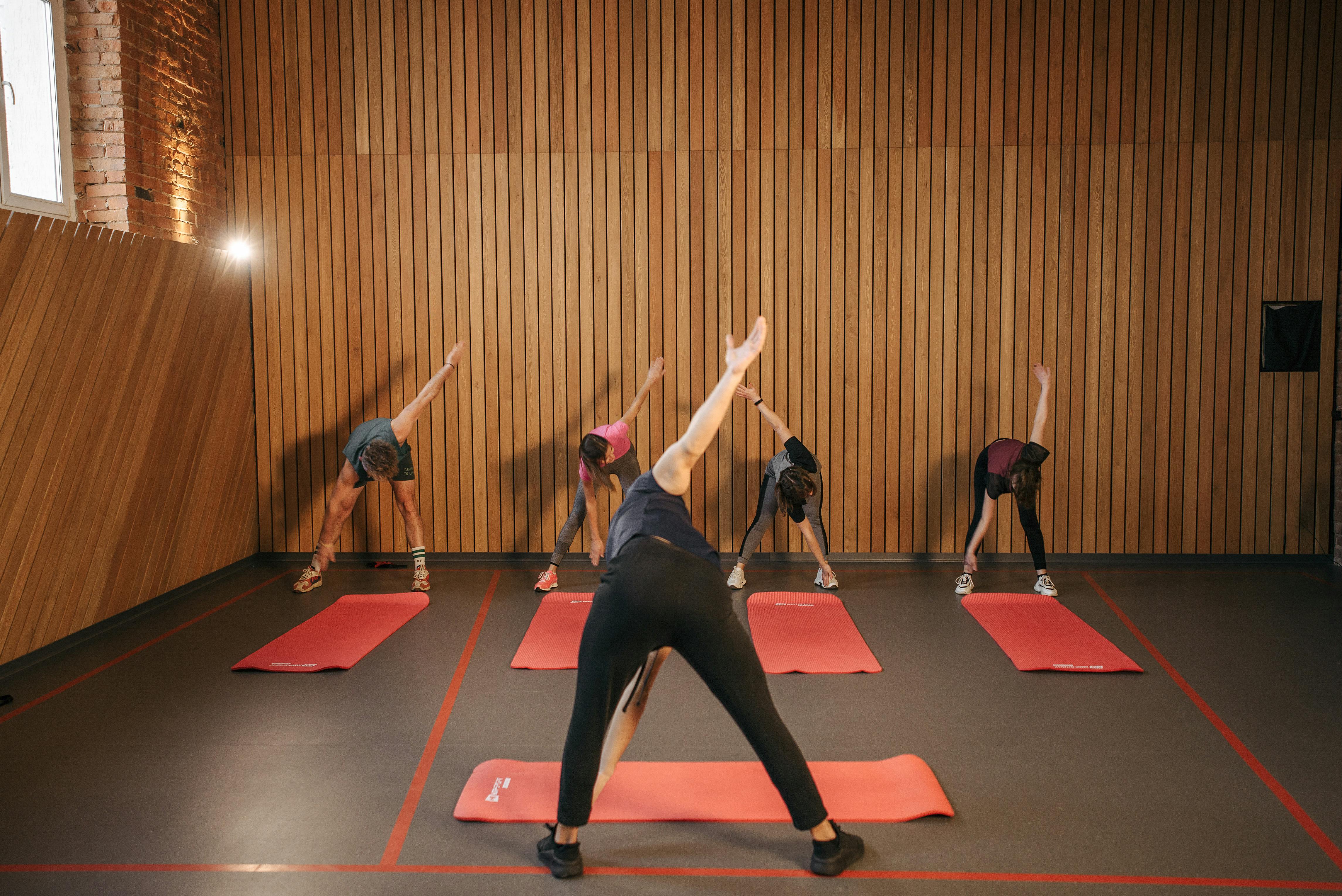Yoga class with diverse adults stretching on mats in a cozy wooden studio.