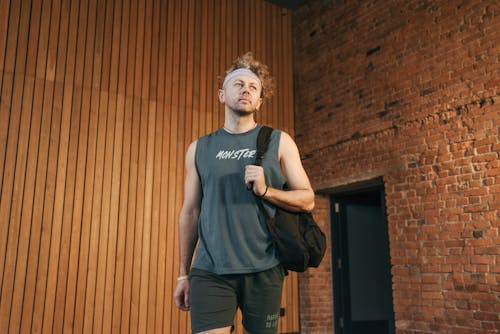Man in Gray Tank Top and Shorts Standing in Front of Brown Wooden Wall