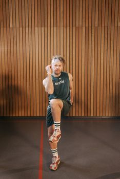 Man in athletic gear performing exercise indoors against wooden wall.