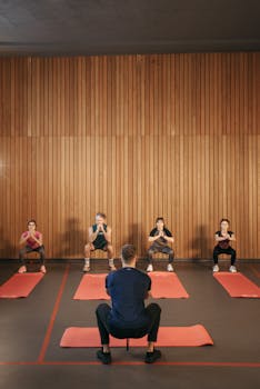 Group of adults doing squats in a yoga studio on red mats against a wooden wall.