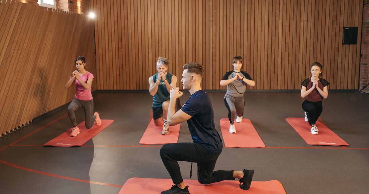 Grupa osób na zajęciach grupowych w jasnej sali fitness — wspólny trening jako element budujący lojalność członków klubu